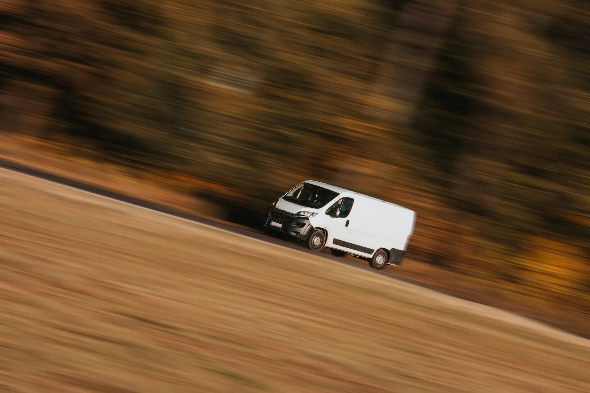 A white van driving along a country road, blurred with motion, representing the ongoing cost of keeping a vehicle on the road
