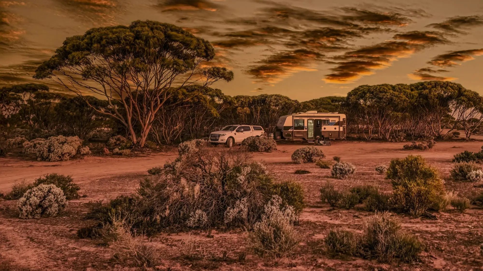 Caravan and 4WD tow vehicle camped in outback mallee scrub at sunset