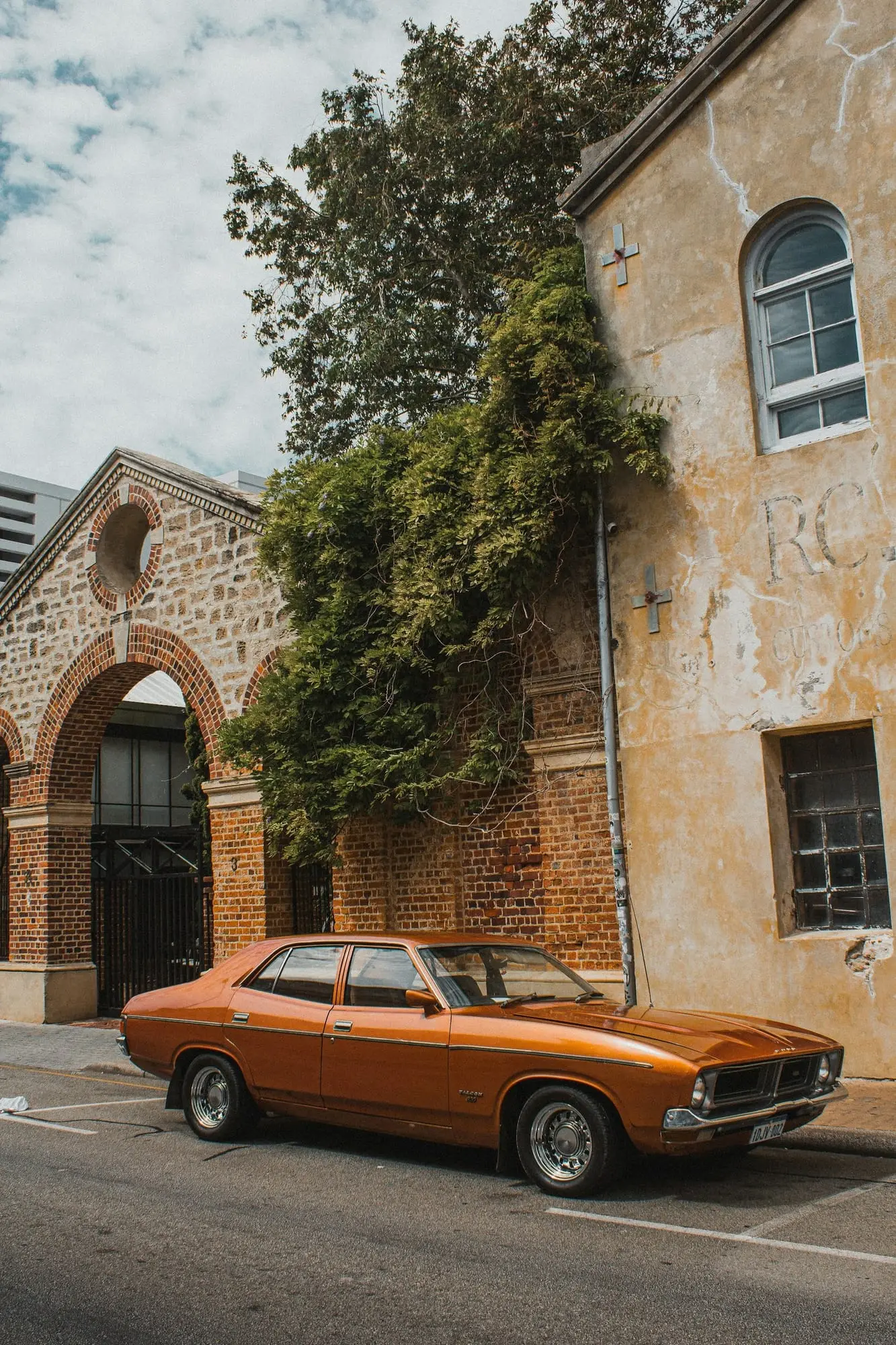 Orange Ford Falcon XB sedan parked beside an old sandstone building