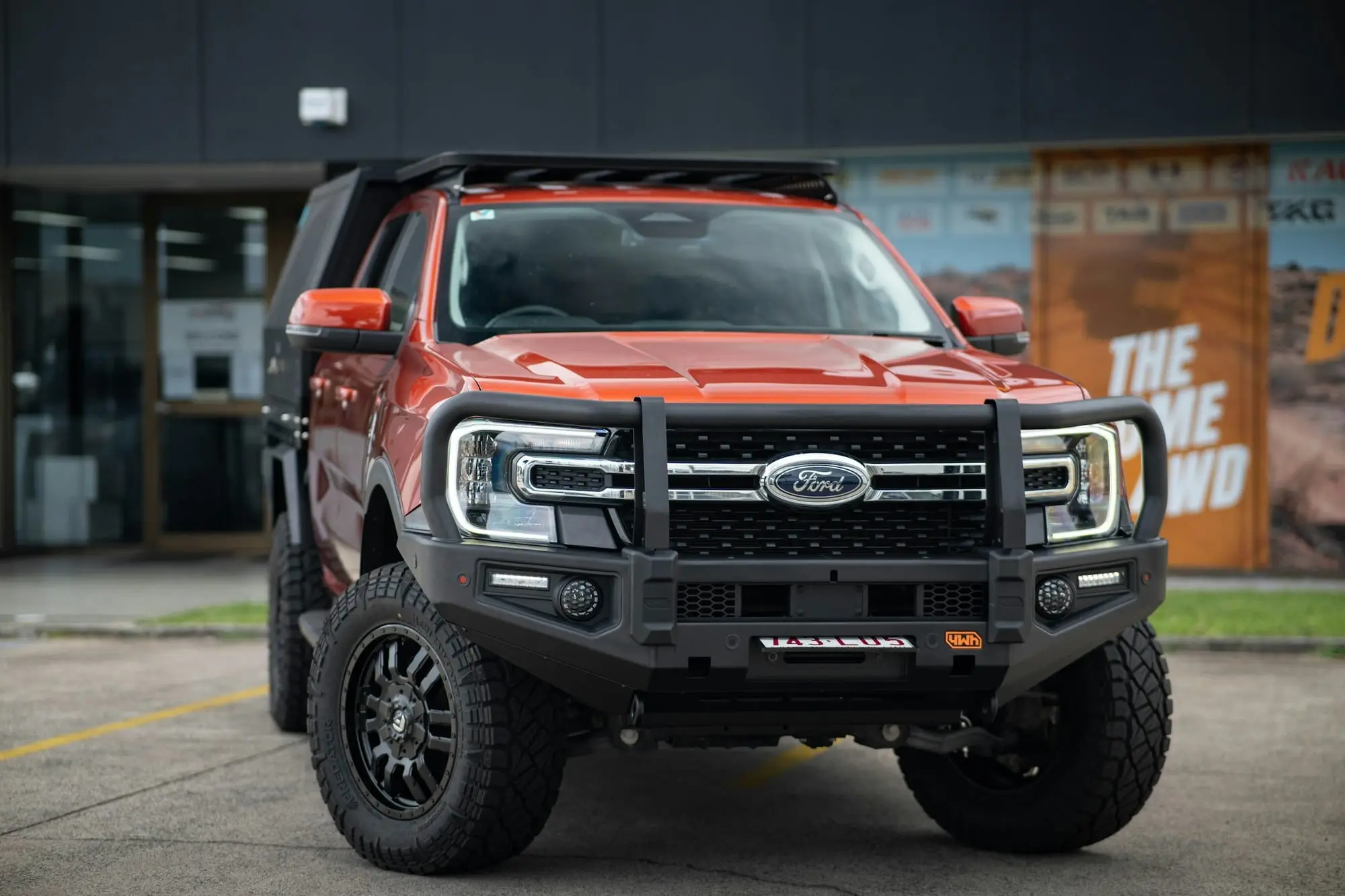 Orange next-generation Ford Ranger with a steel bullbar, front-on outside a 4WD accessories shop