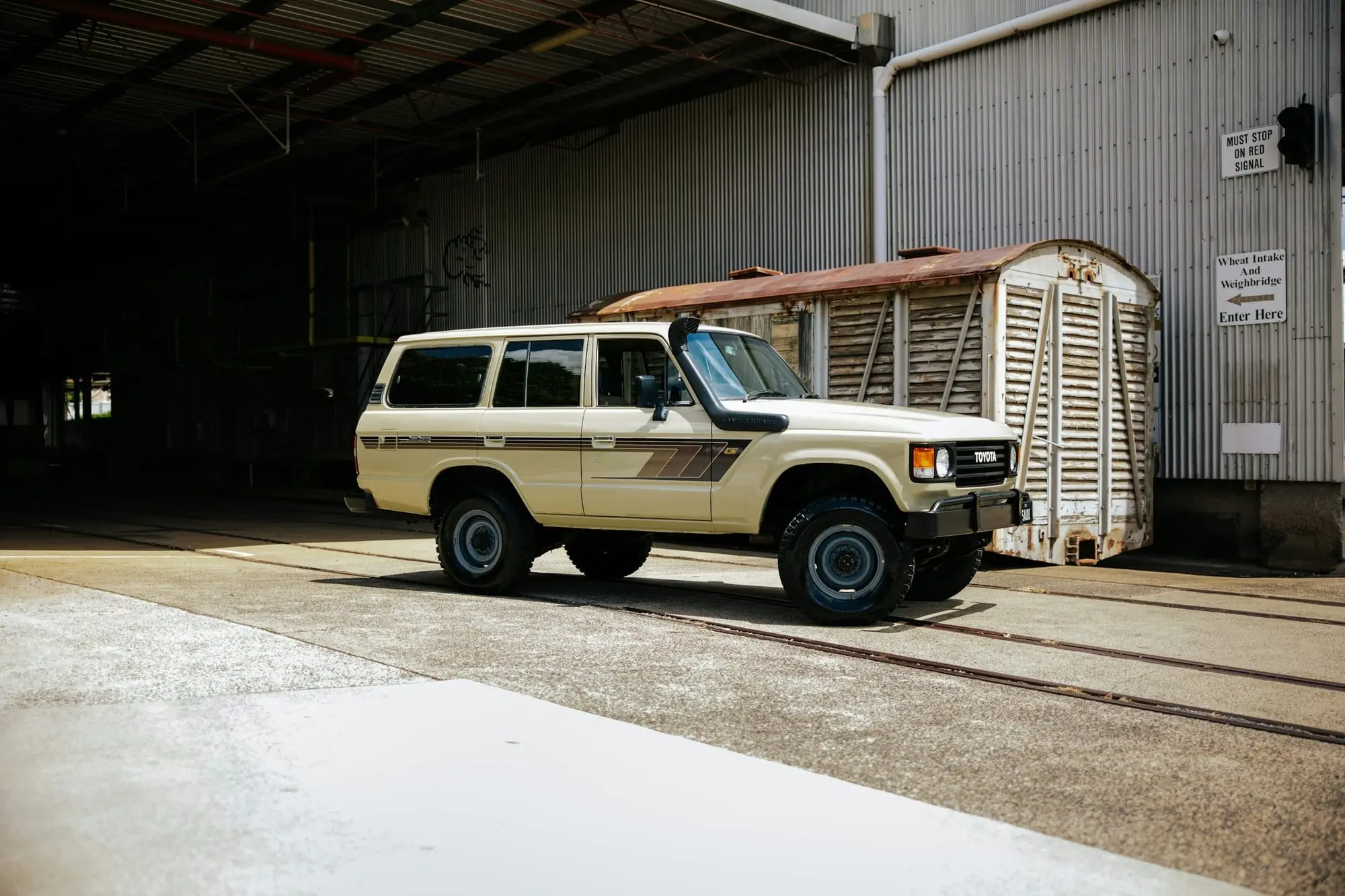 Cream Toyota LandCruiser 60 Series with snorkel parked beside an old railway shed