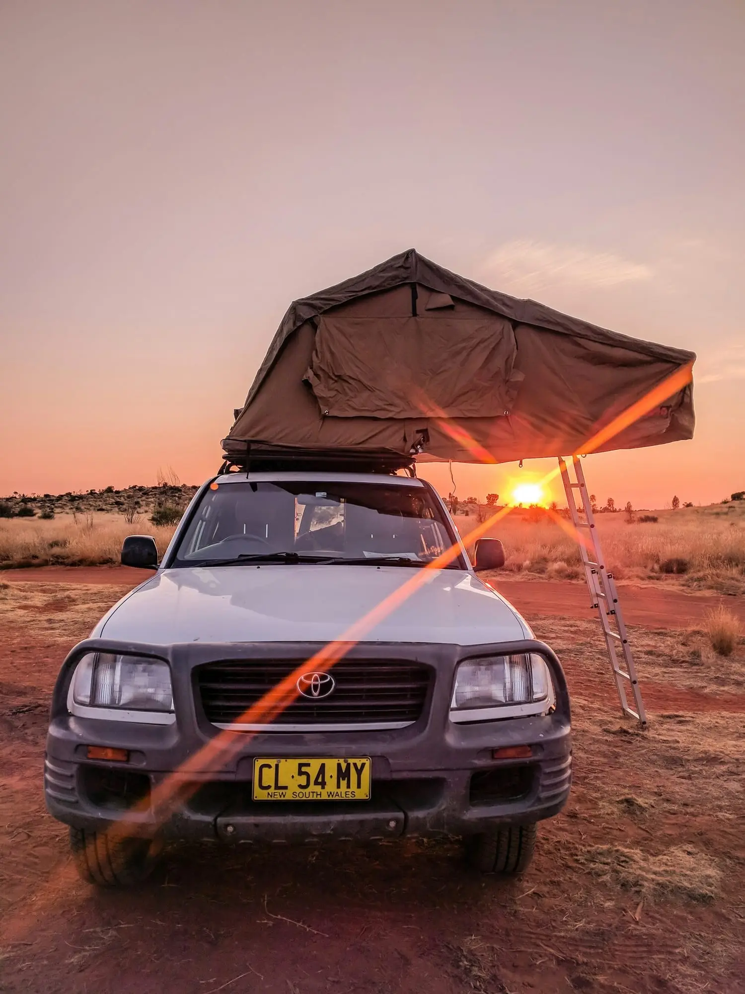 Toyota LandCruiser 100 with a rooftop tent set up on red dirt at an outback sunset